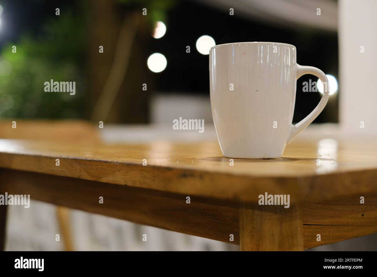 Selective shot of a white mug on a wooden table with bokeh or blurred background Stock Photo