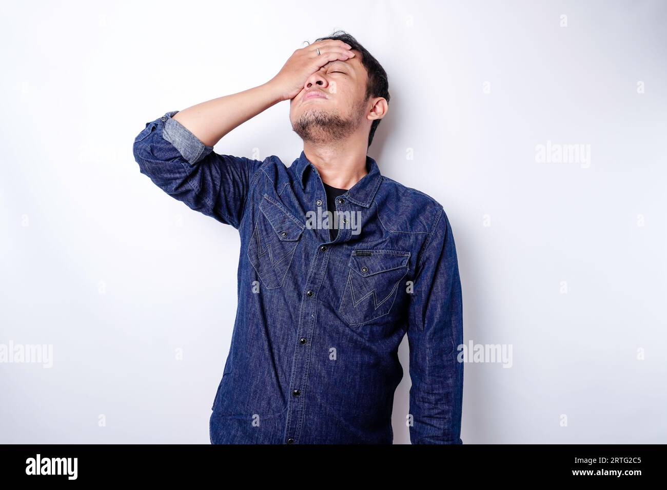 A portrait of an Asian man wearing a blue shirt isolated by white background looks depressed Stock Photo