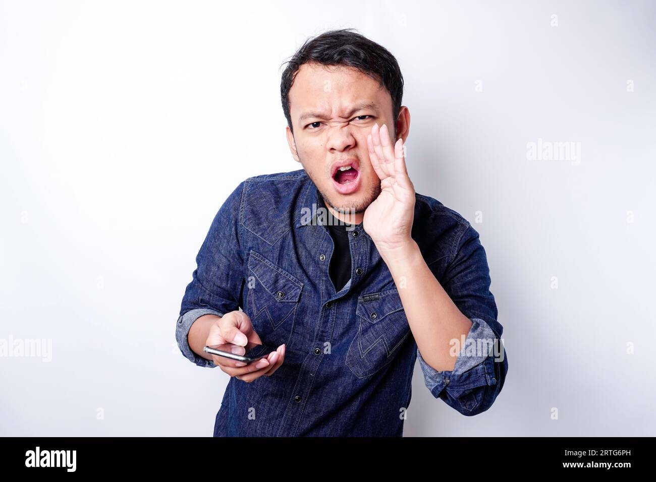 The angry and mad face of Asian man in blue shirt holding his phone ...