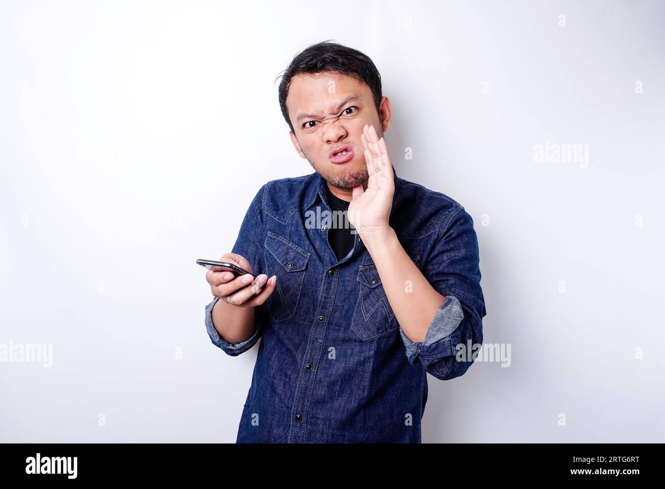 The angry and mad face of Asian man in blue shirt holding his phone ...