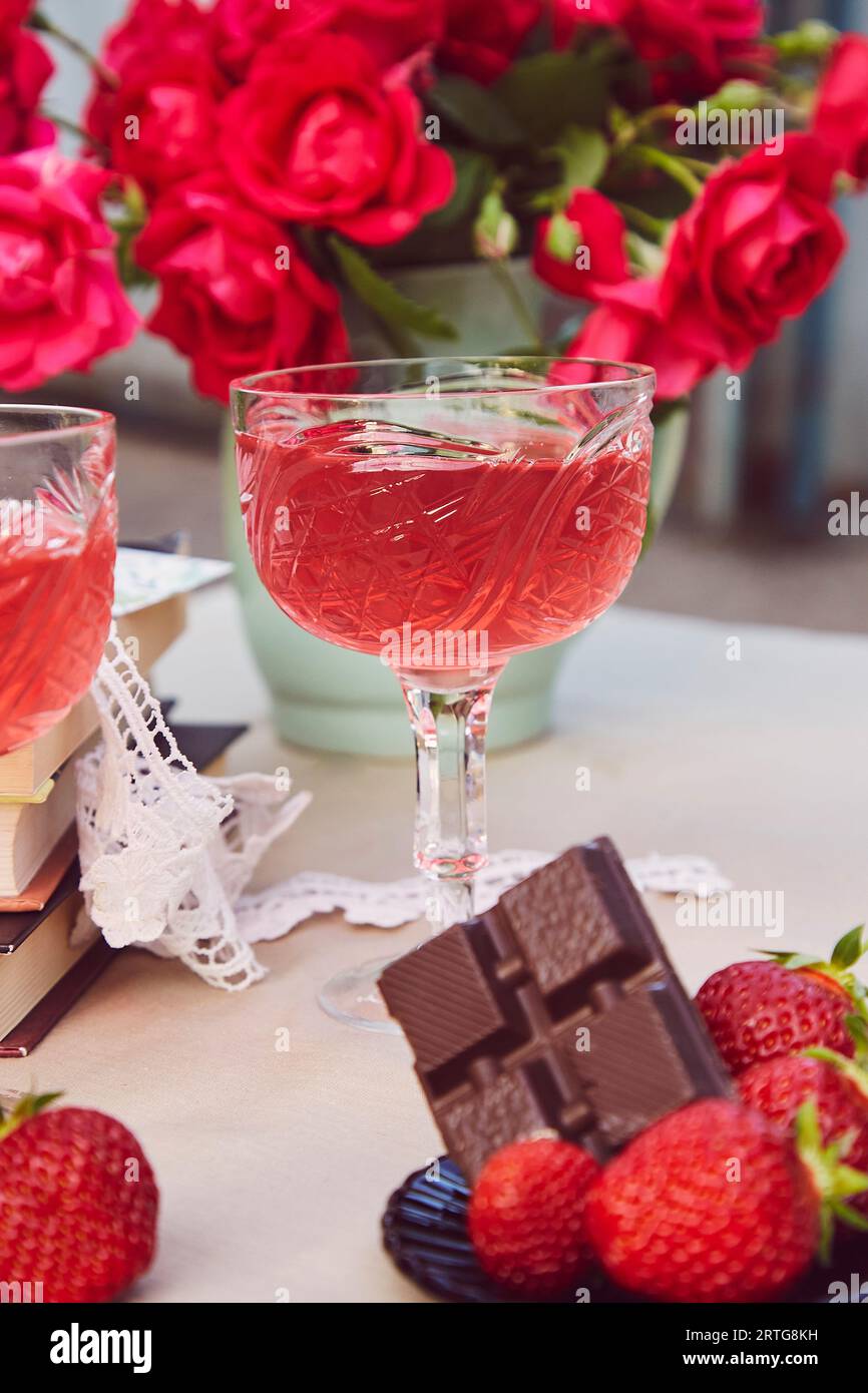 Romantic summer table settings. Couple glasses of red strawberry wine, strawberry and chocolate. Roses bouquet Stock Photo