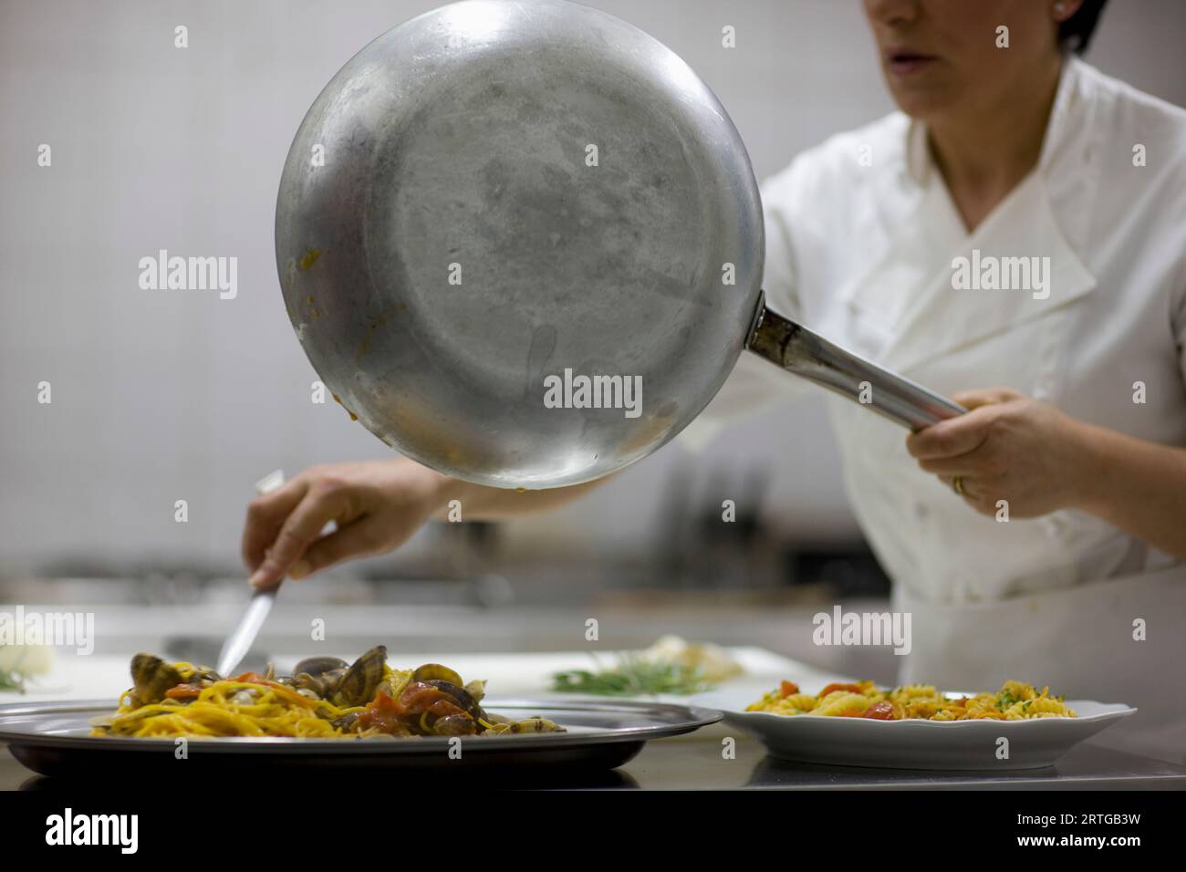 Woman chef holding a frying pan and preparing seafood pasta for service Stock Photo