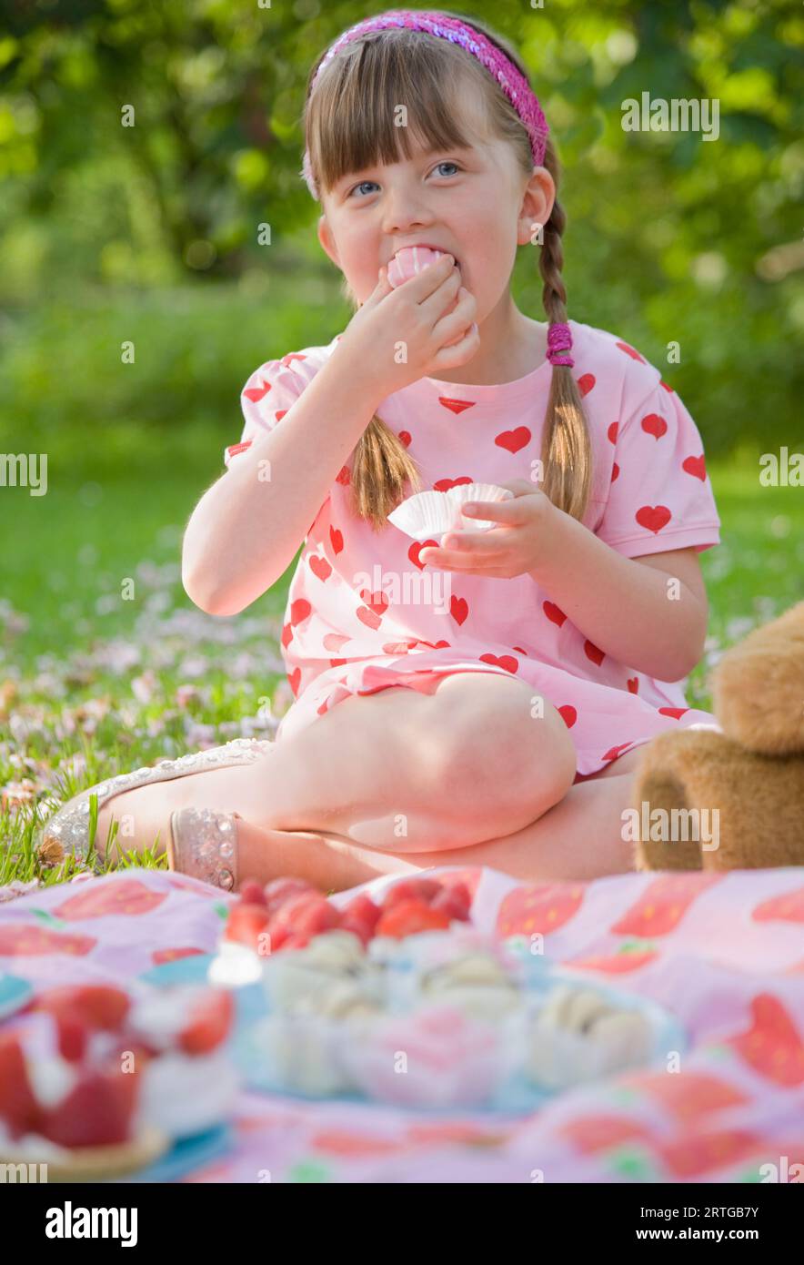 Young girl sitting in a garden smiling and eating a cupcake Stock Photo