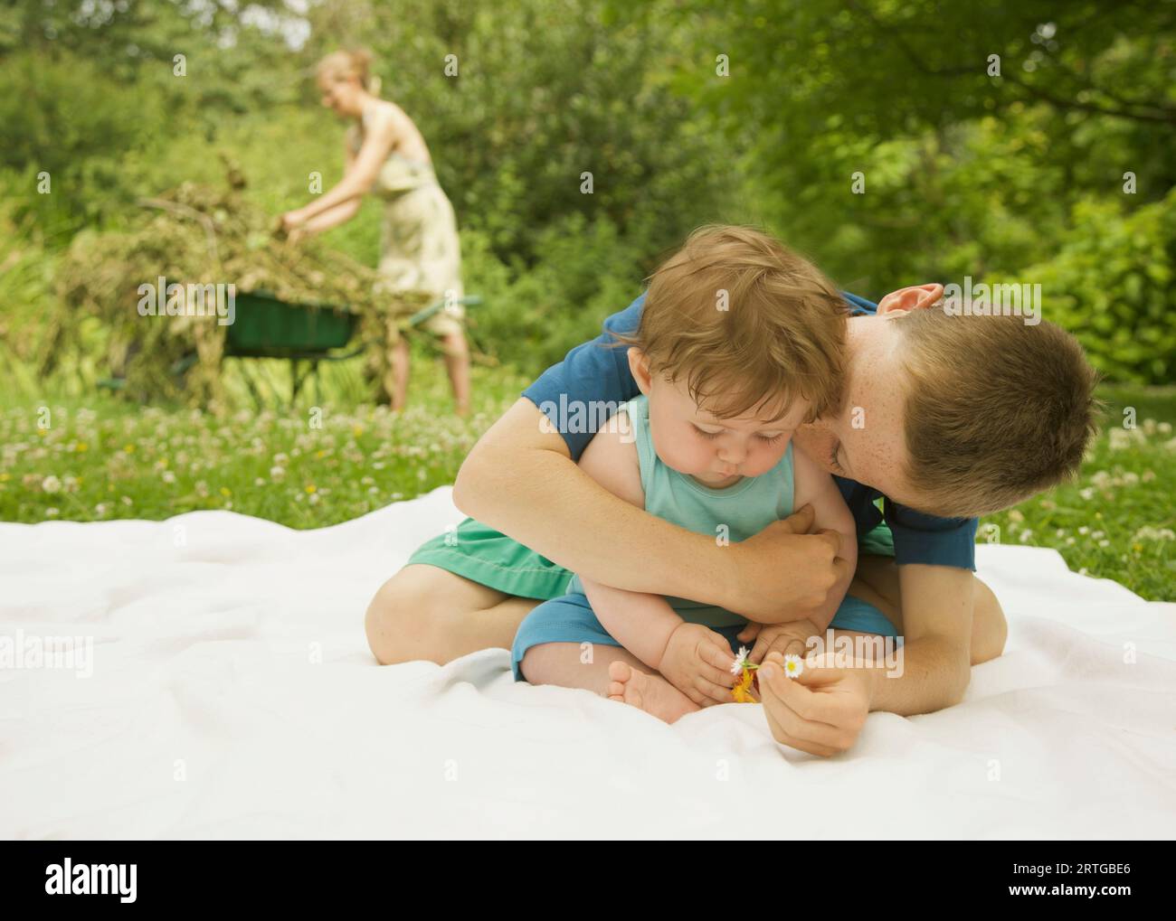 Young boy sitting in a garden embracing a kissing his baby brother Stock Photo