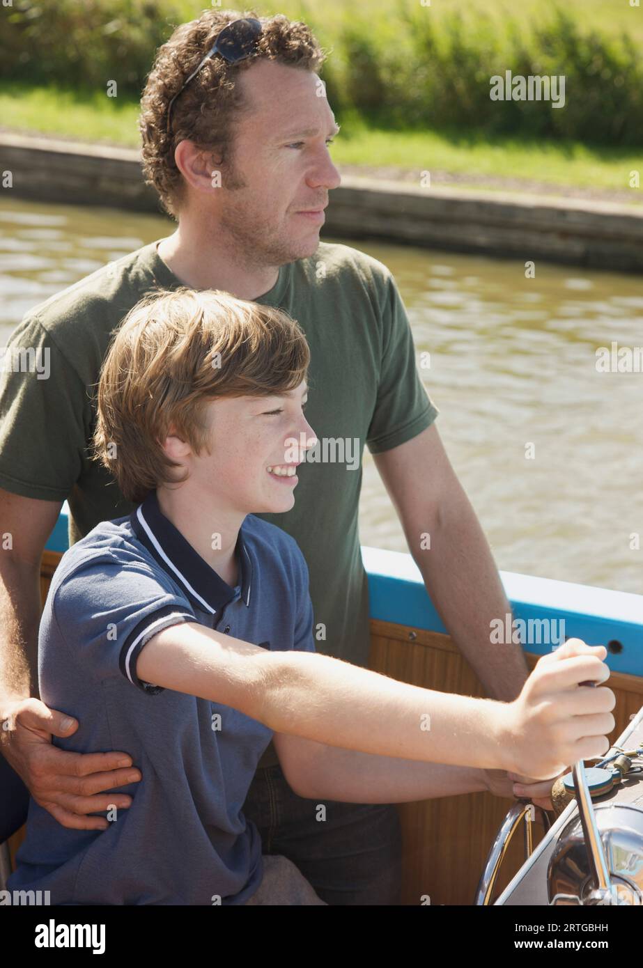 Man and smiling teenaged boy steering a boat Stock Photo