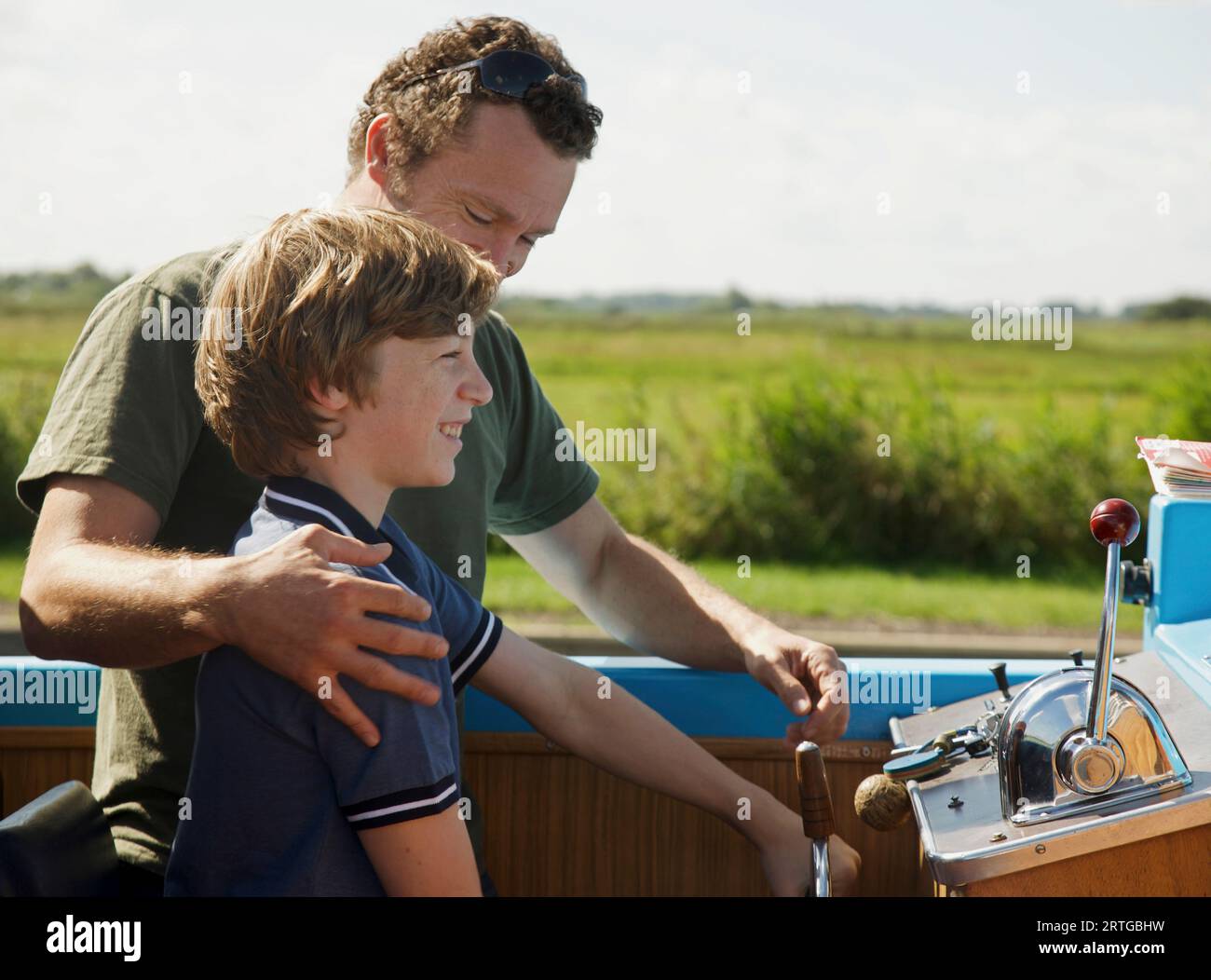 Man and smiling teenaged boy steering a boat Stock Photo