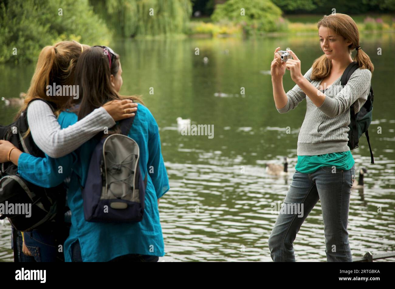 Teenaged girl taking photograph of two women by a lake Stock Photo