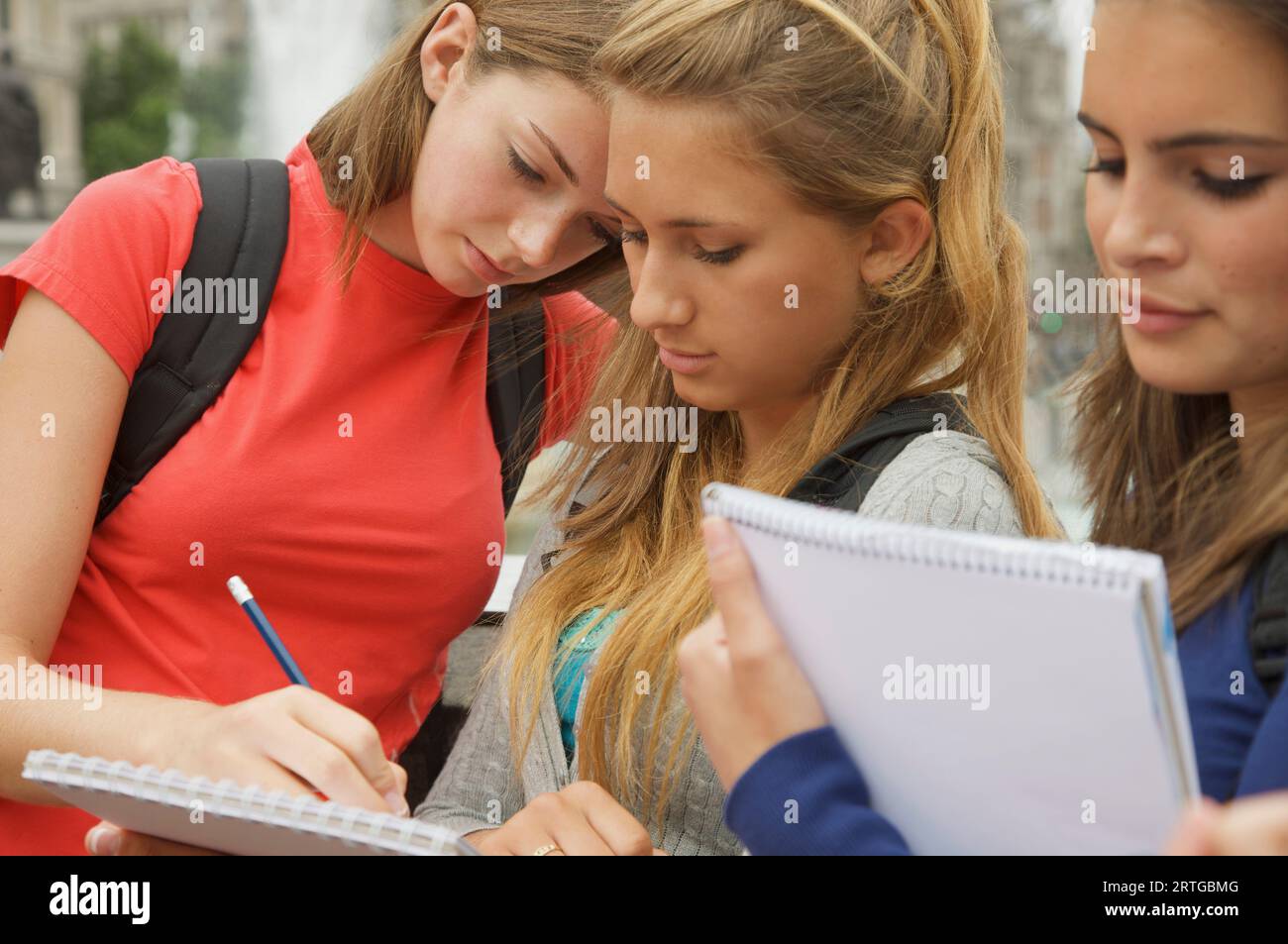 Three teenaged girls reading, writing and holding note pads Stock Photo