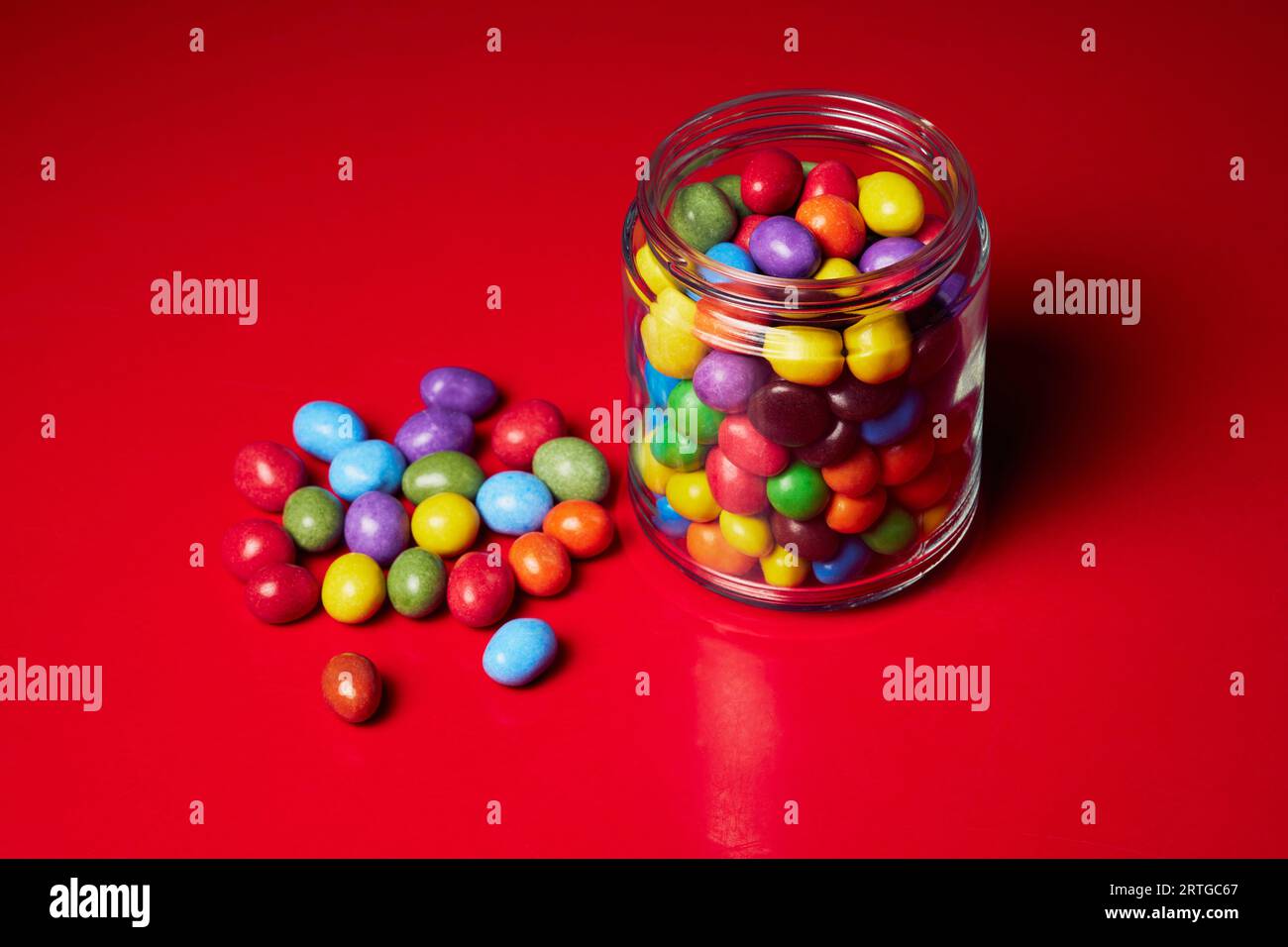 Still life multicolored candy in glass jar on red background Stock Photo