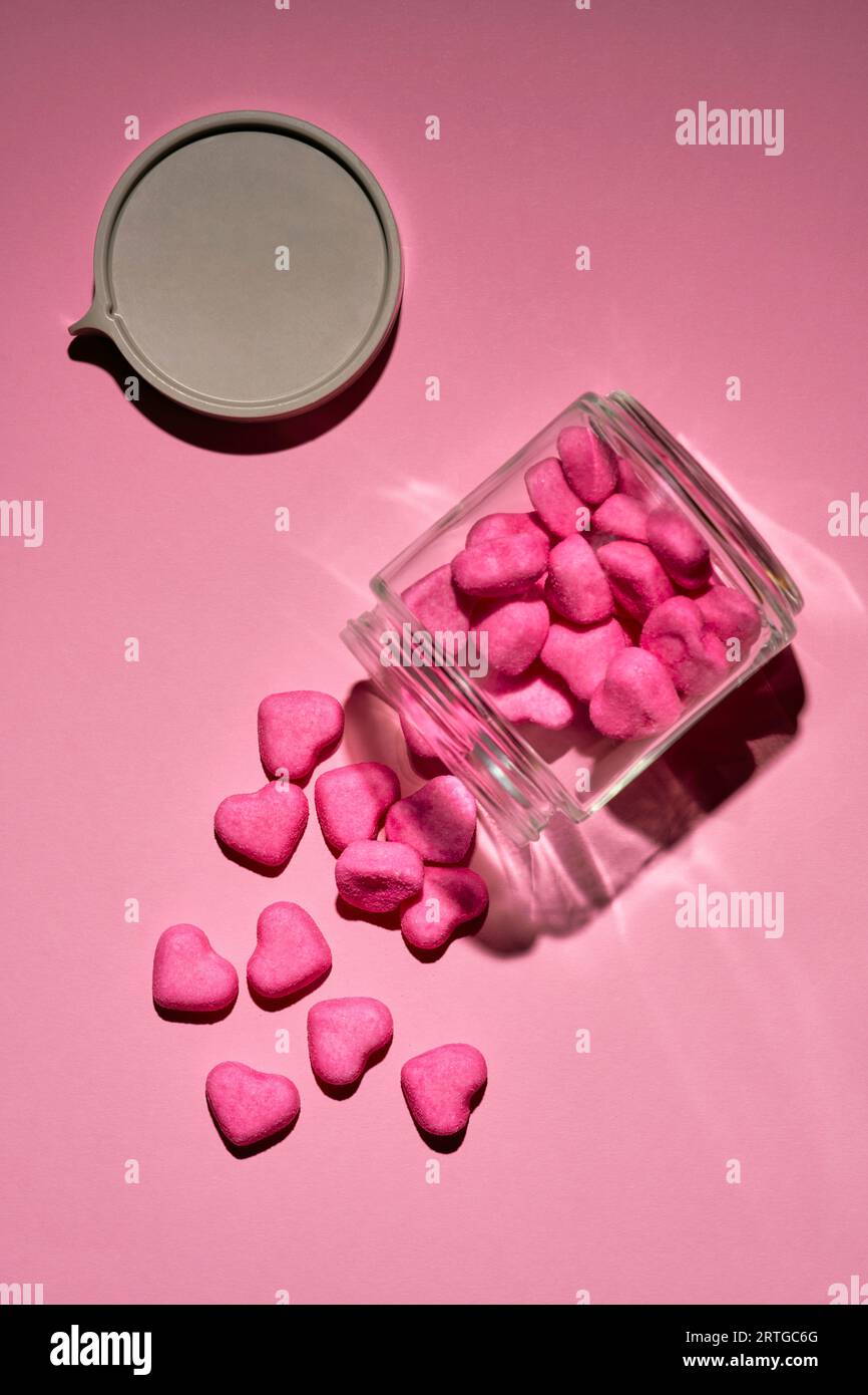 Pink candy hearts spilling from glass jar on pink background Stock Photo