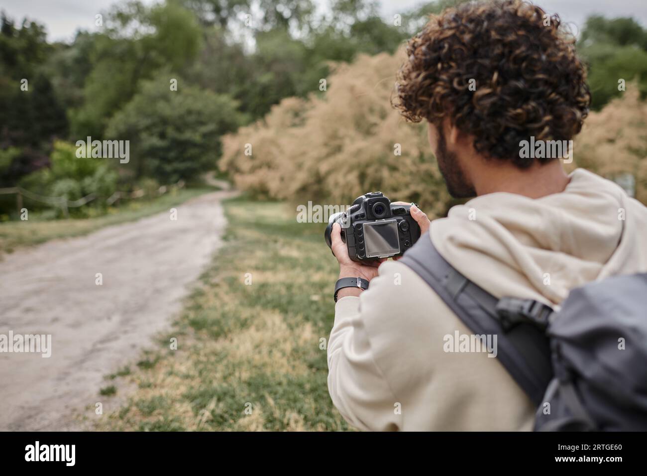 Photographer Back back view of curly indian photographer with backpack taking photo on ...