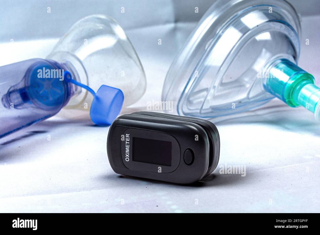 Digital pulse oximeter photographed on a white background in high key, next to an inhaler mask. Medical instruments. Stock Photo