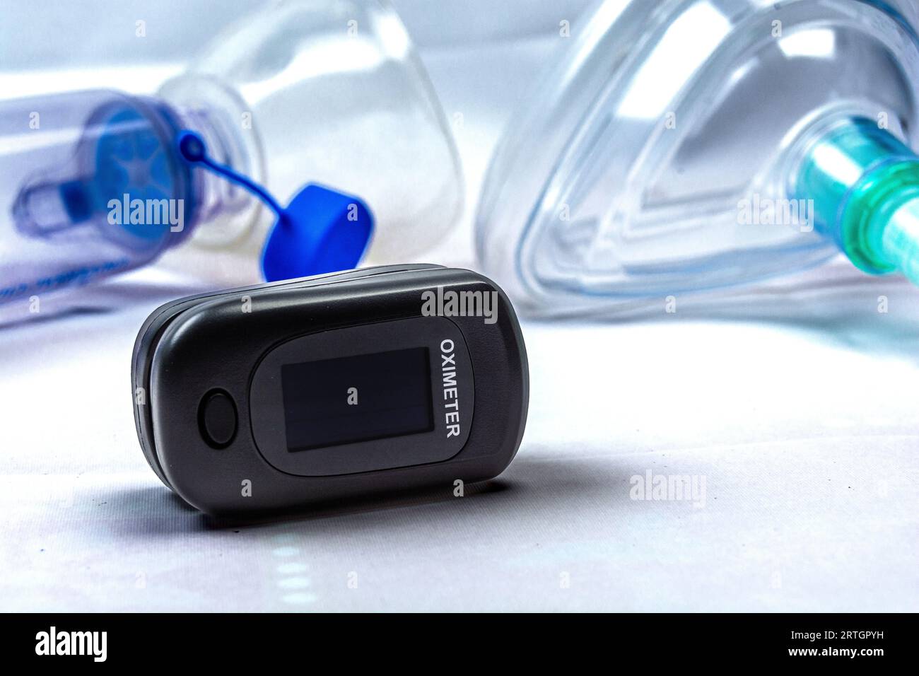 Digital pulse oximeter photographed on a white background in high key, next to an inhaler mask. Medical instruments. Stock Photo
