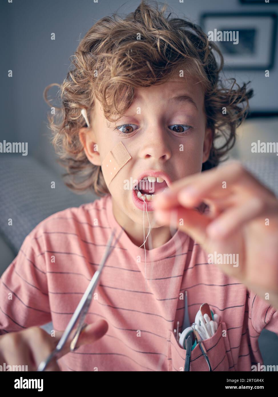 Scared boy in t shirt with cotton swabs cutting thread on milk tooth ...
