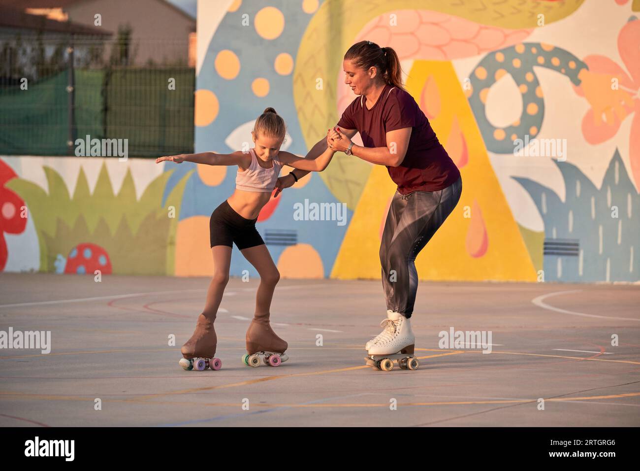 Serious full body girl training element spread eagle in roller skates  looking down during young female coach holding hand and helping saved  balance Stock Photo - Alamy