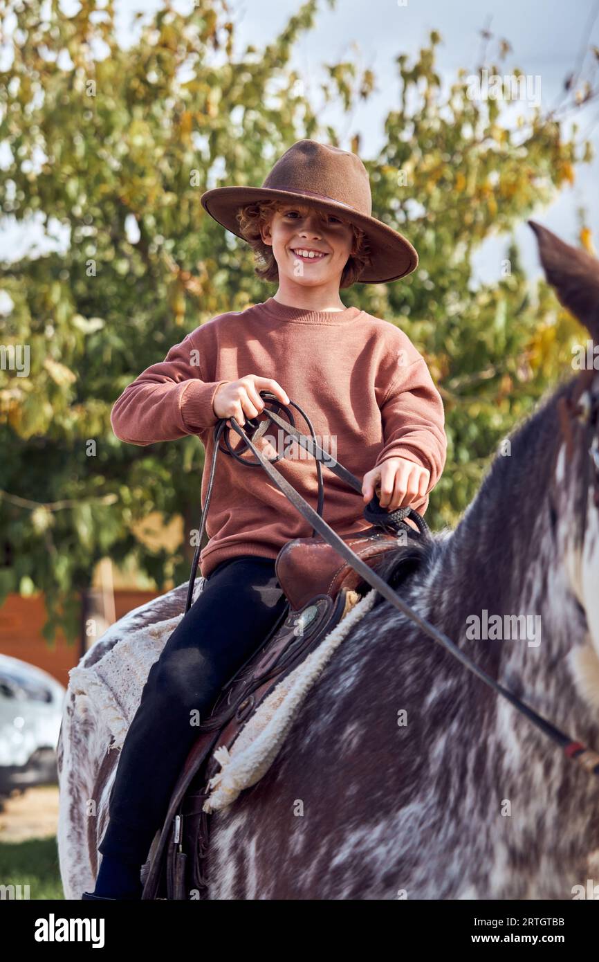 Boy in hat riding his brown mottled horse Stock Photo