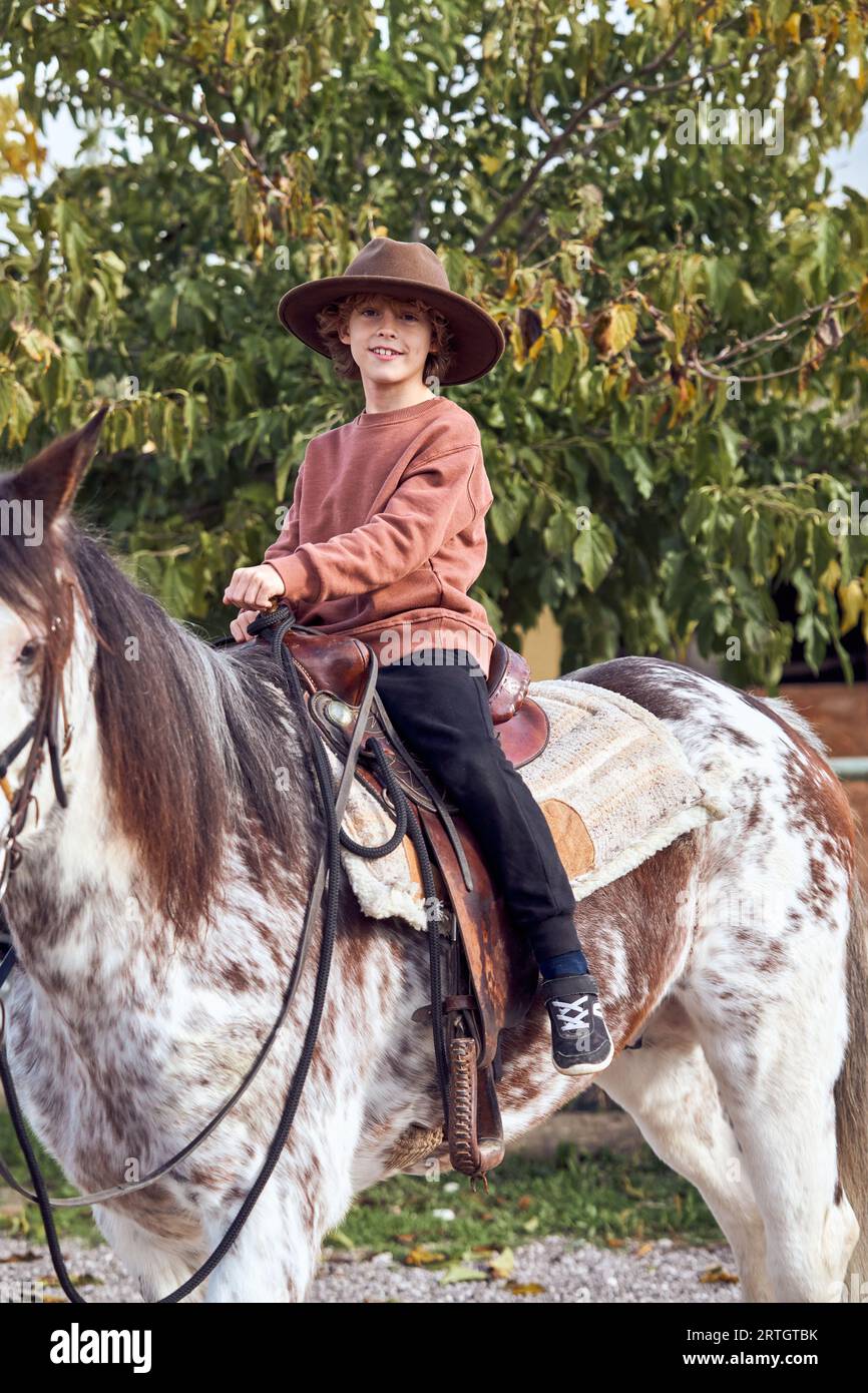 Boy in hat riding his brown mottled horse Stock Photo