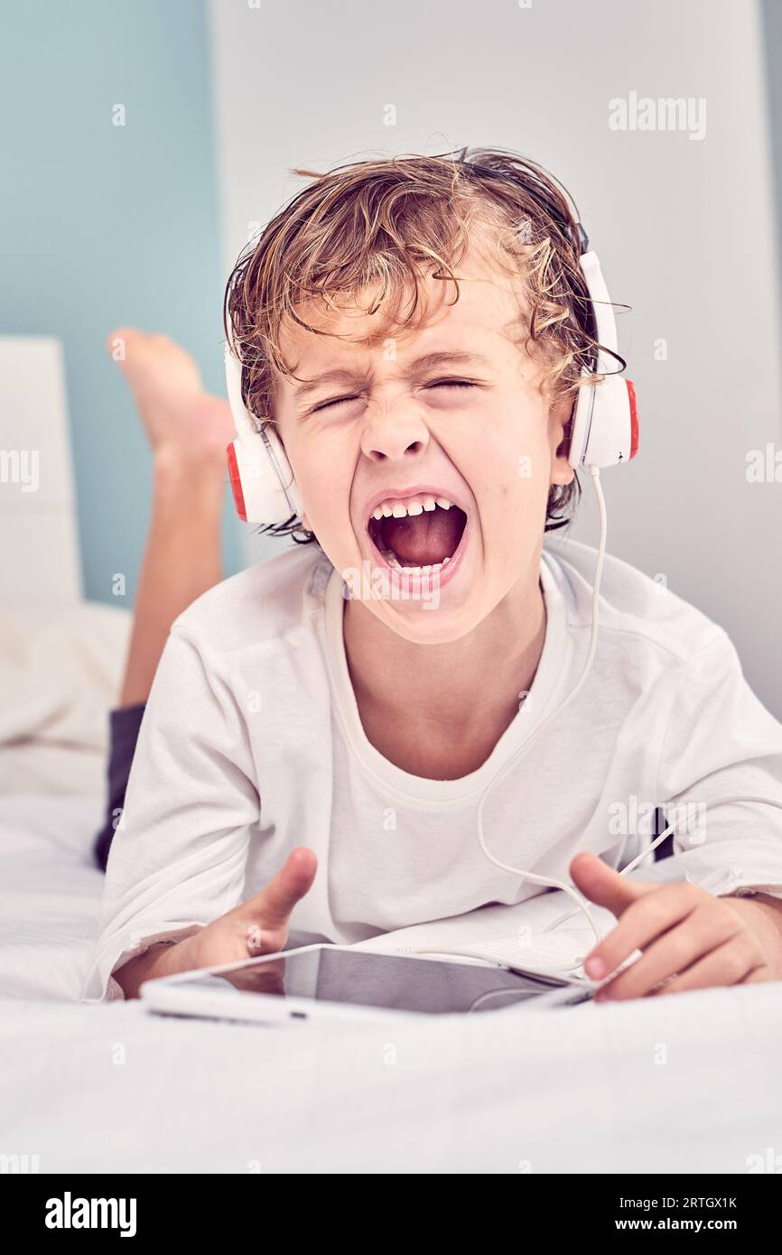 Barefoot boy with wet hair lying on bed and screaming loudly while
