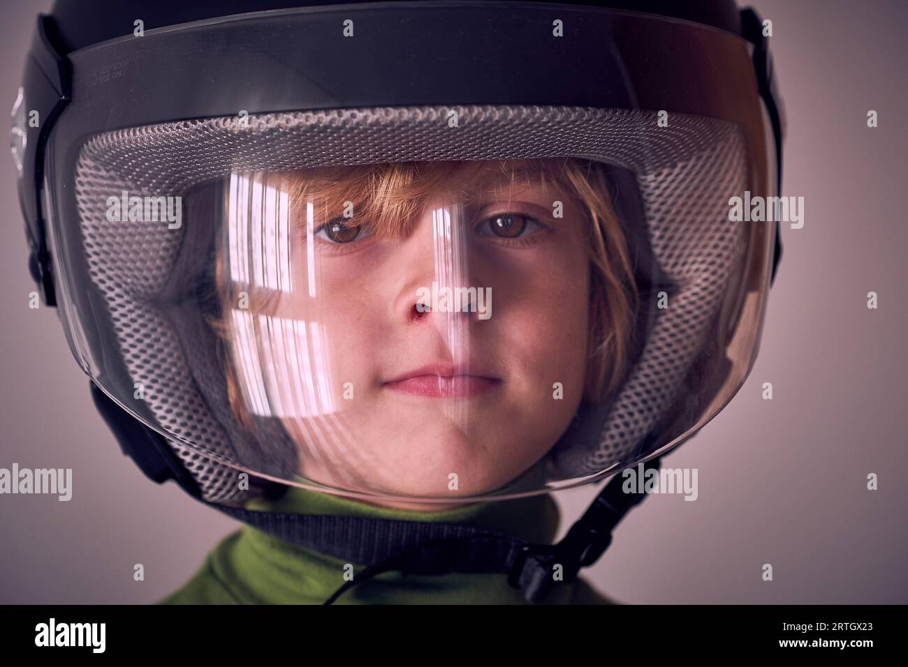 Portrait of cute little kid with blond hair and brown eyes wearing protective helmet with transparent plastic front and looking at camera Stock Photo