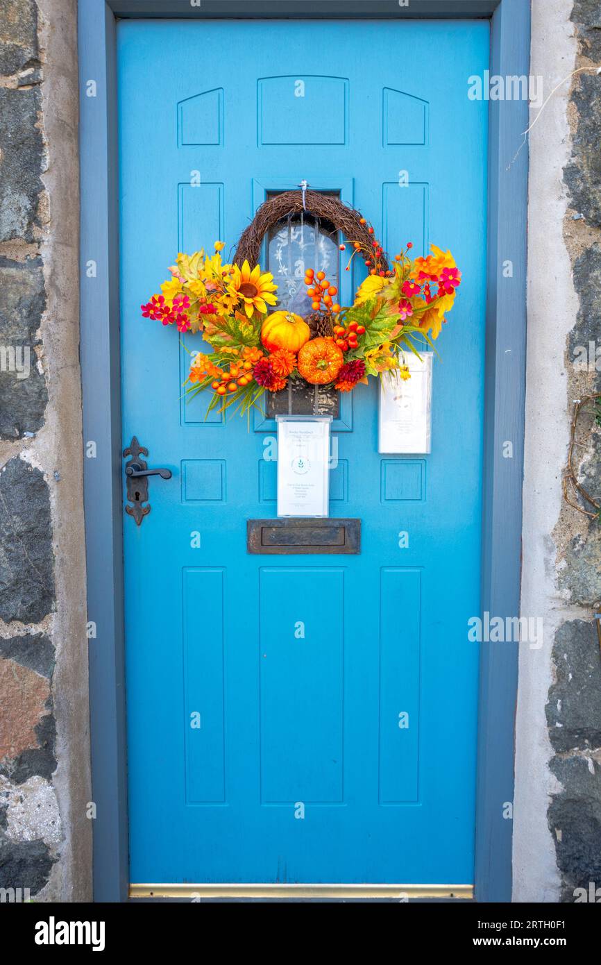 Colourful wreath of flowers, berries and small pumpkins attached on a pale blue front door. Stock Photo
