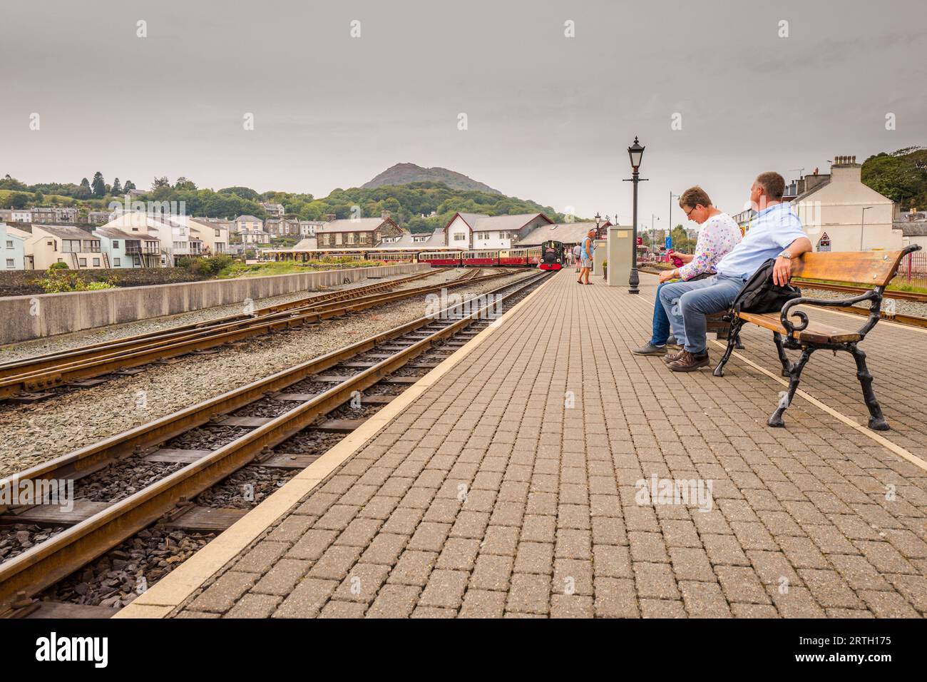 Passengers wait seated on the platform at Porthmadoc railway station for the steam train. Stock Photo