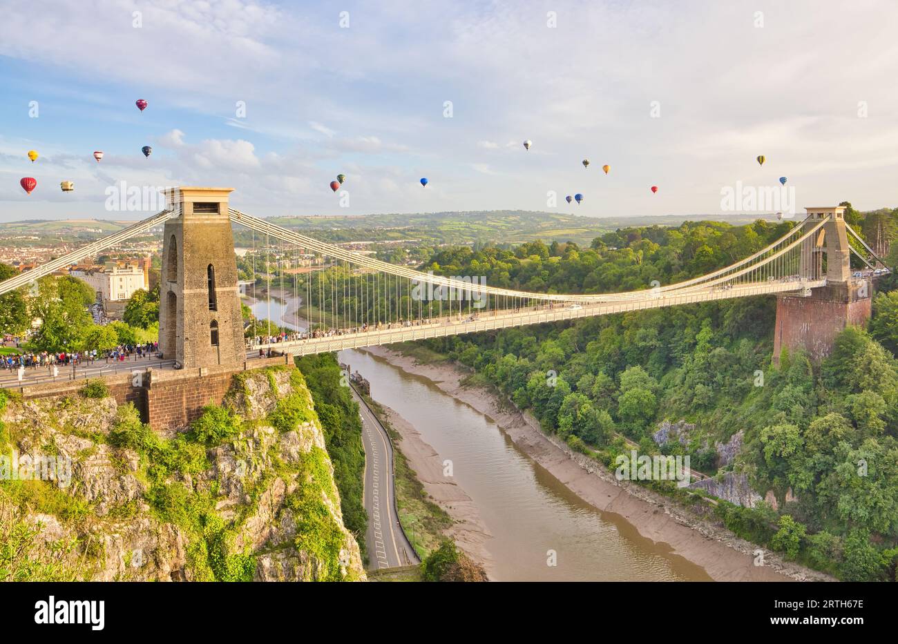 Vibrantly coloured hot air balloons fill the full width of the sky as they soar over Clifton Suspension bridge during the Hot Air Balloon Fiesta. Stock Photo