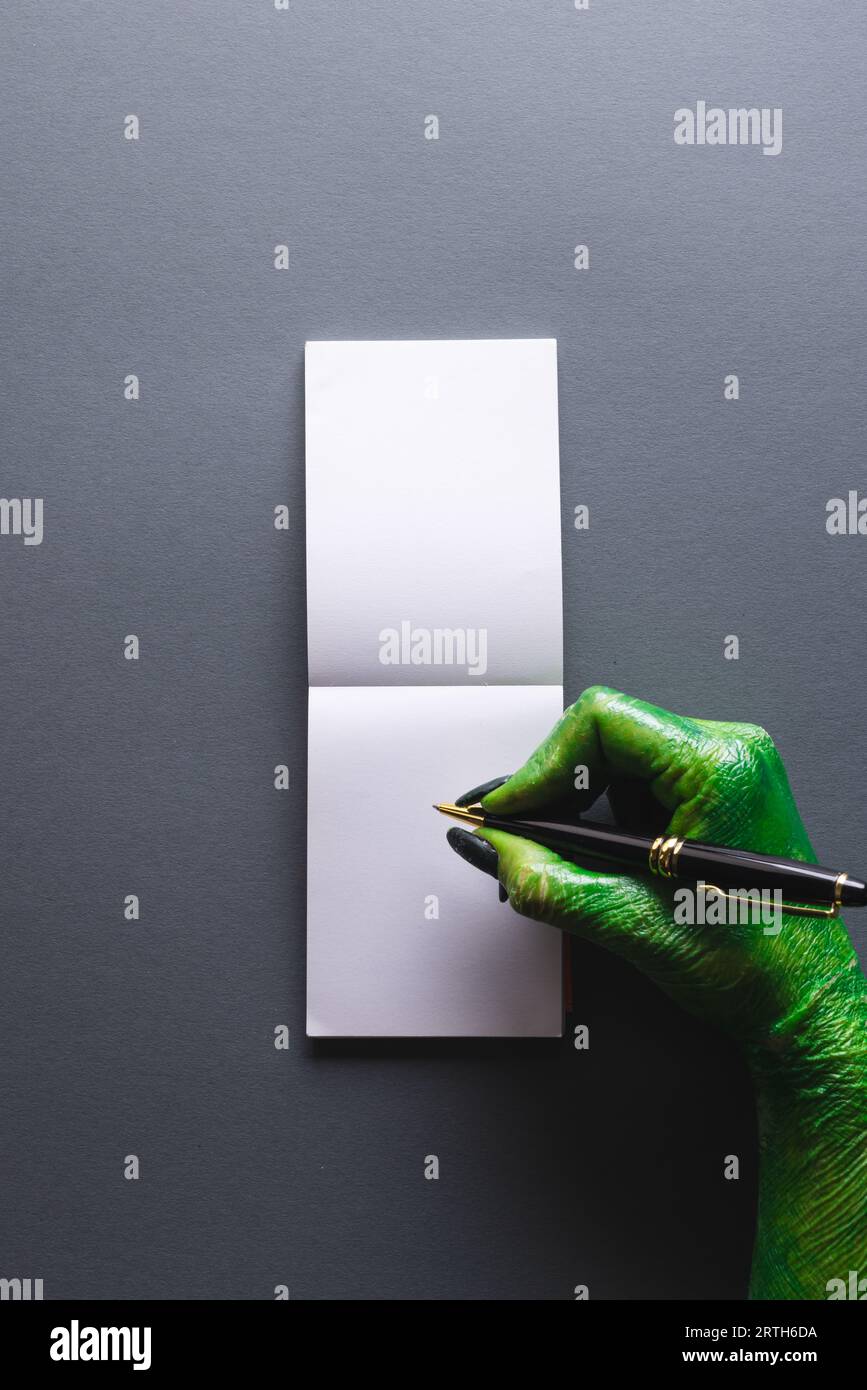 Vertical image of green monster hand writing notebook with copy space on grey background Stock Photo