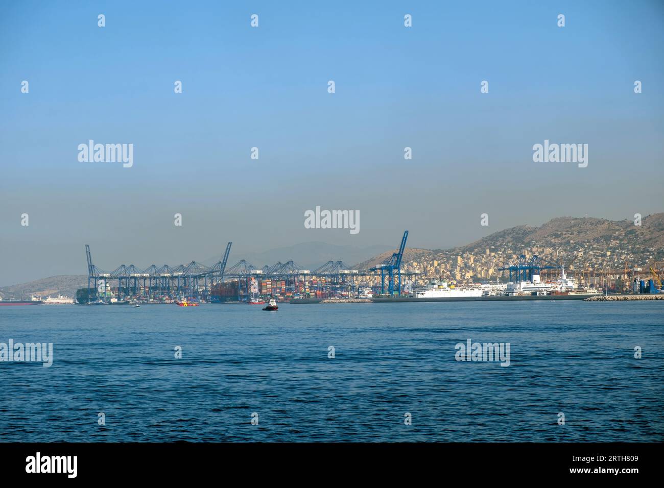 Piraeus port, Attica Greece. Industrial zone, container terminal, moored cargo ship for loading or unloading. Mediterranean sea, blue sky background. Stock Photo