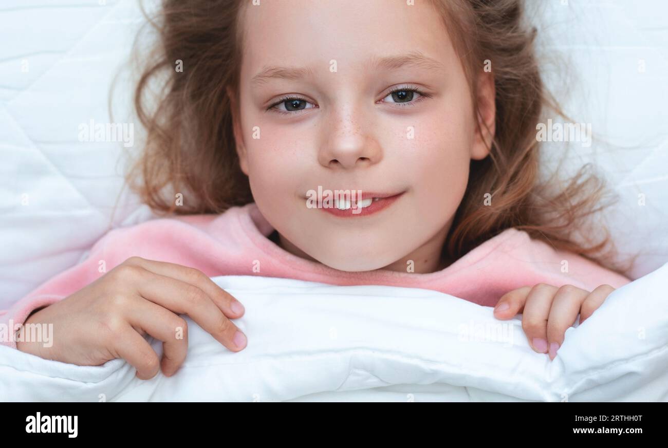 Cute adorable caucasian blond little girl lying in bed on white pillow