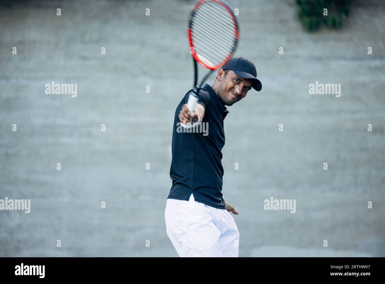 Young tennis player playing on a hard court and hitting a ball during a match Stock Photo