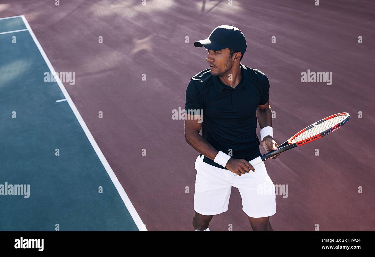 Tennis player in sportswear and a cap standing on a hard court preparing to receive the serve. Tennis player during a tennis match. Stock Photo