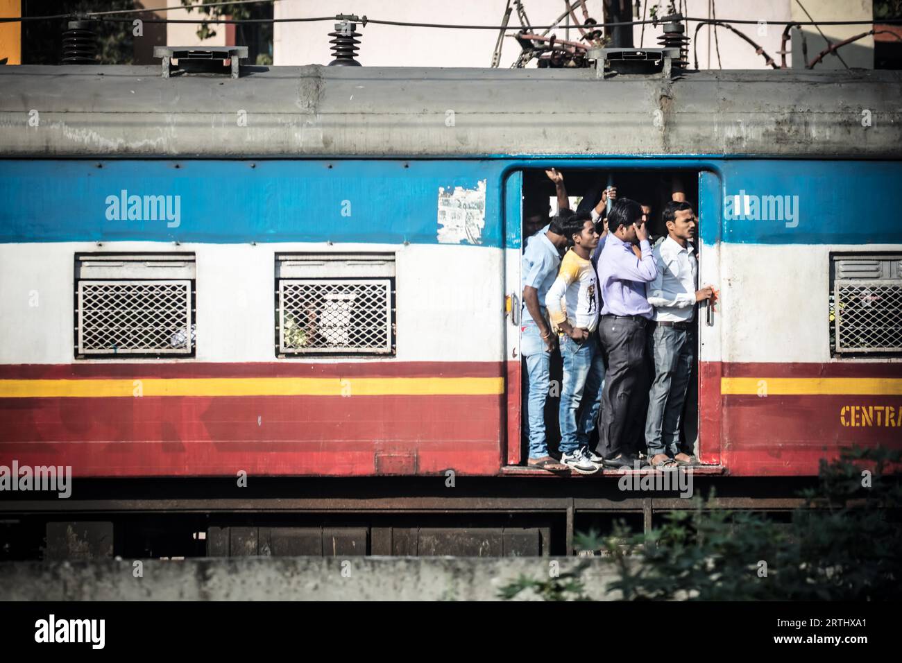 MUMBAI, INDIA, November 10 2017: Commuters on a crowded train hang at the door of an old train in Mumbai, India Stock Photo