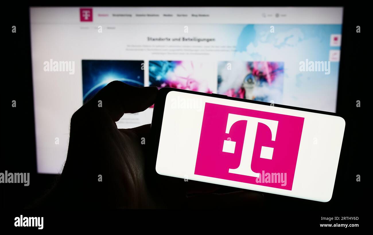Person holding smartphone with logo of telecommunications company Deutsche Telekom AG on screen in front of website. Focus on phone display. Stock Photo