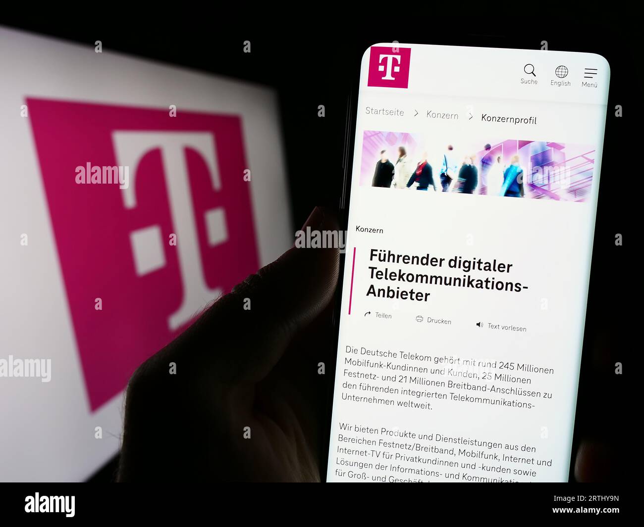 Person holding cellphone with webpage of telecommunications company Deutsche Telekom AG on screen with logo. Focus on center of phone display. Stock Photo