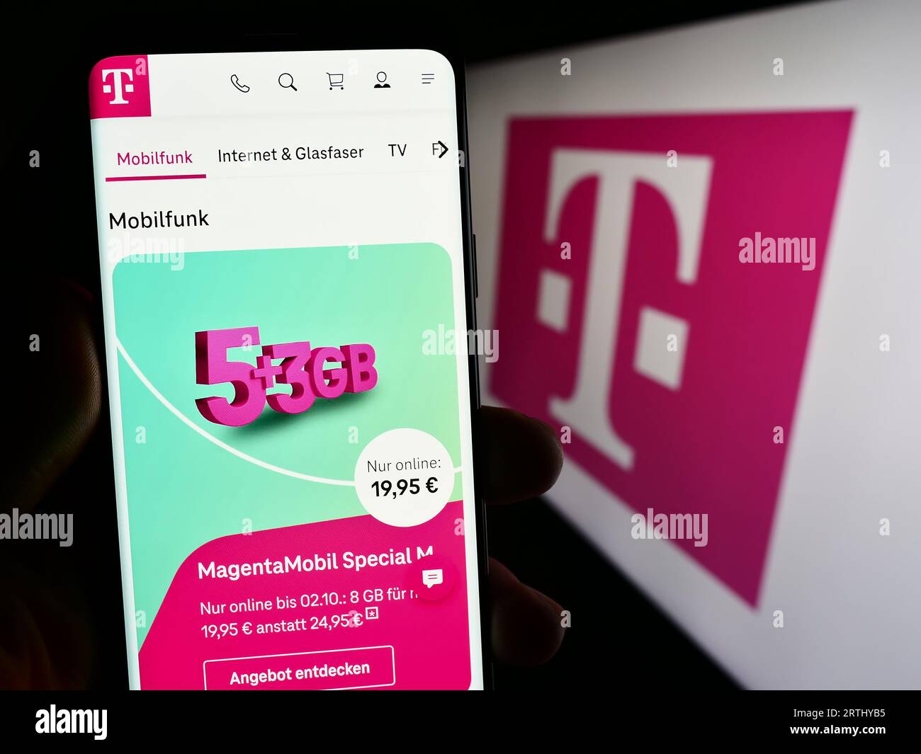 Person holding mobile phone with web page of telecommunications company Deutsche Telekom AG on screen with logo. Focus on center of phone display. Stock Photo