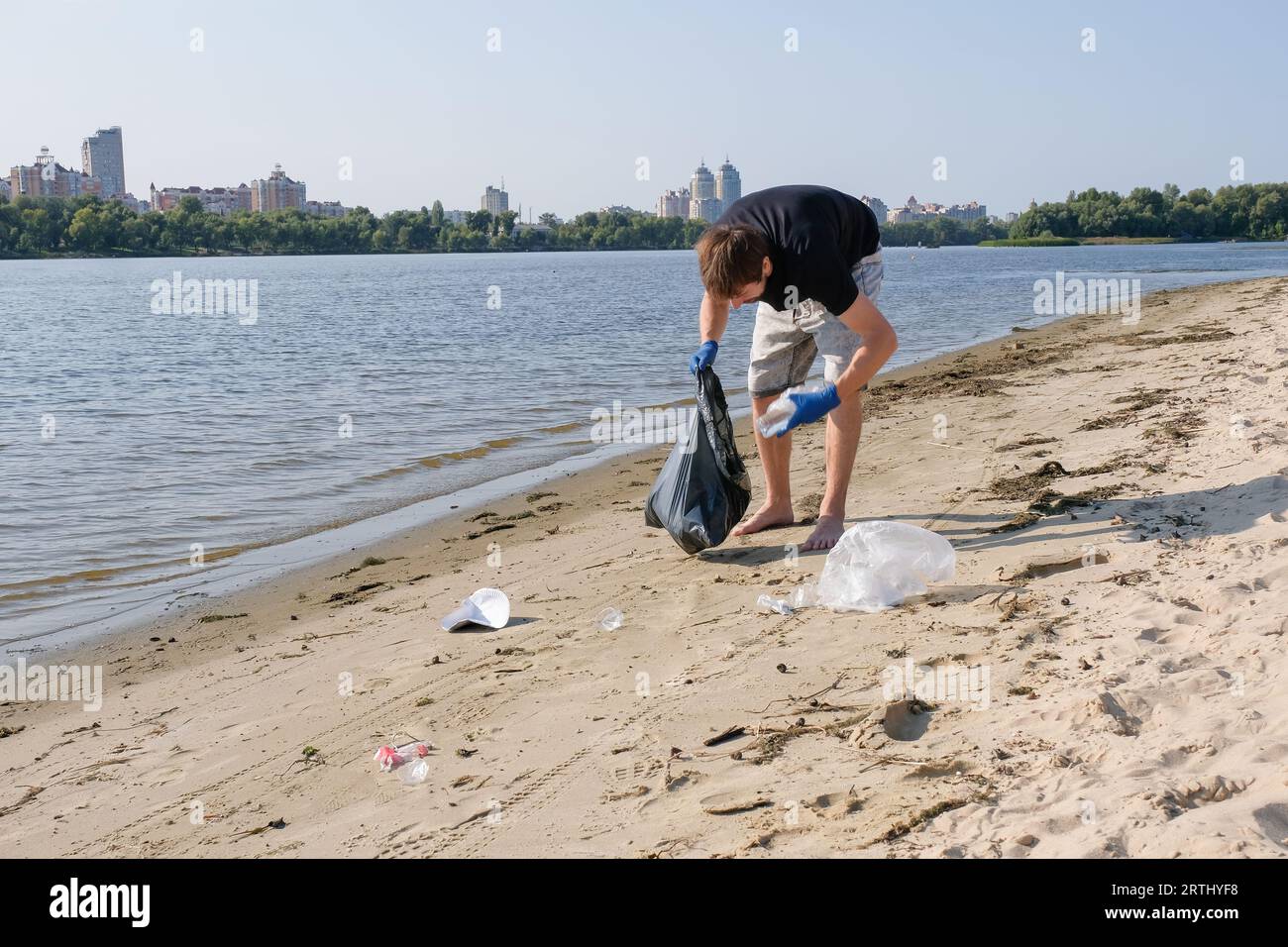Volunteer man with trash bag collects rubbish on a public beach