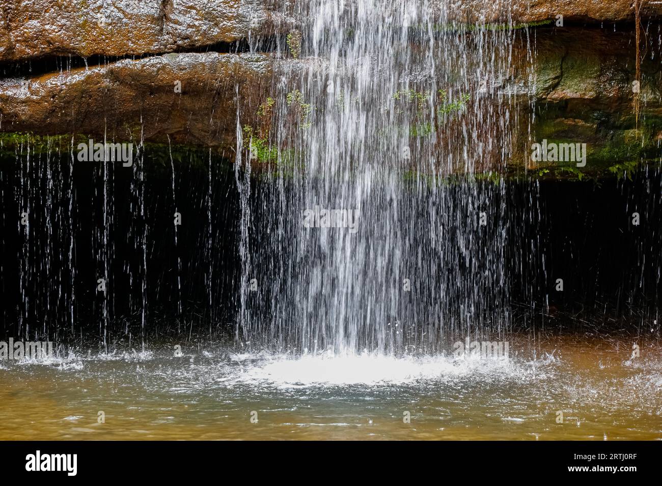 Water dropping down with splash over a rock into a pond Stock Photo