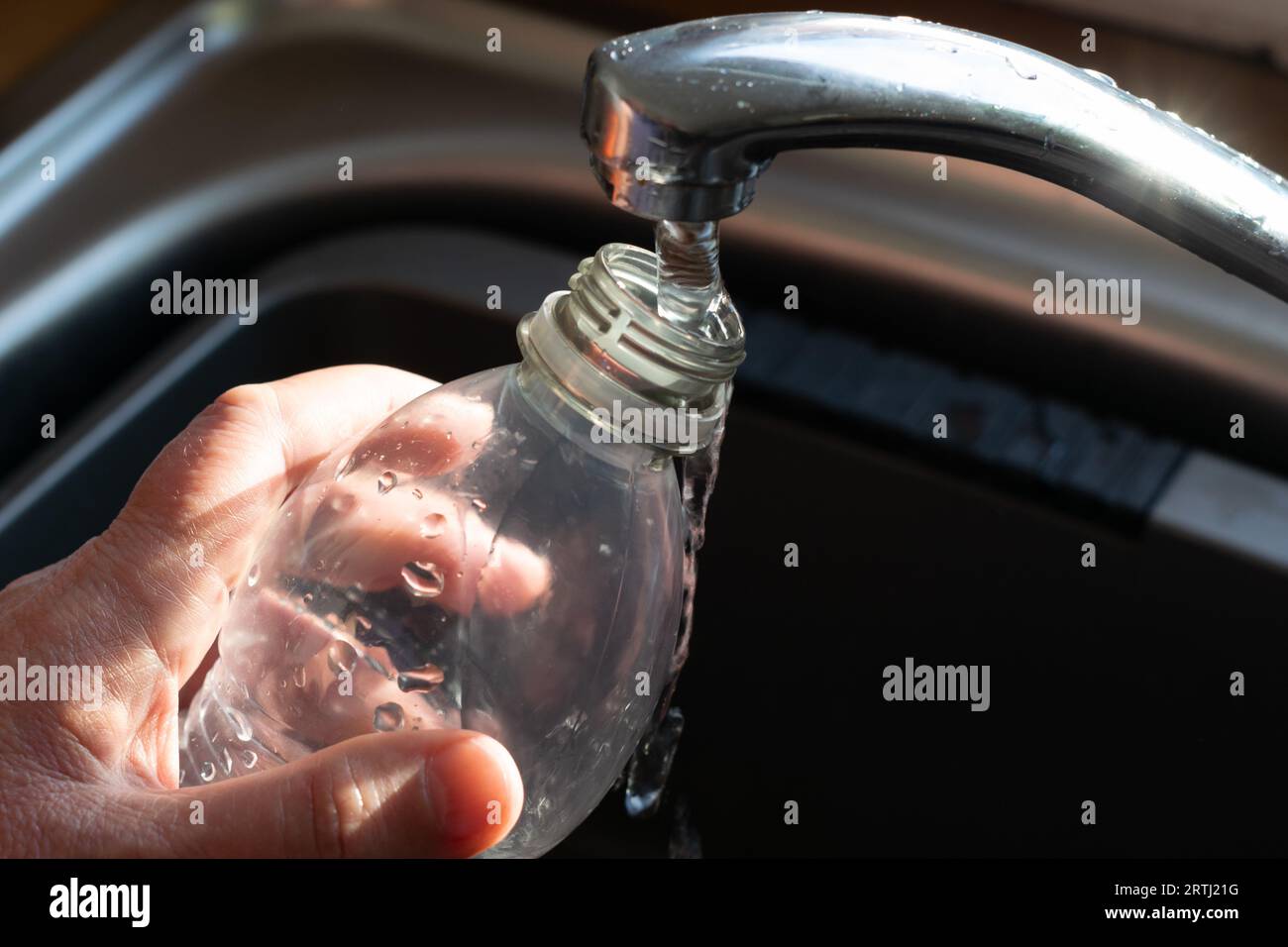 Refilling a plastic water bottle from mixer tap. Concept recycling, cost of living crisis, tap water purity. Stock Photo