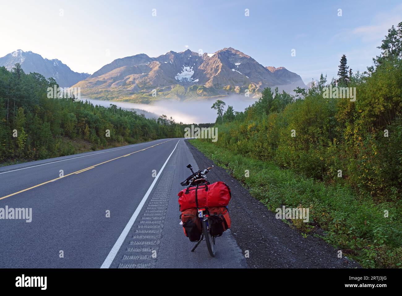 Bicycle on a straight, traffic-free road, fog, foliage colouring and snow-covered mountains, Richardson Highway, Alakska, USA Stock Photo