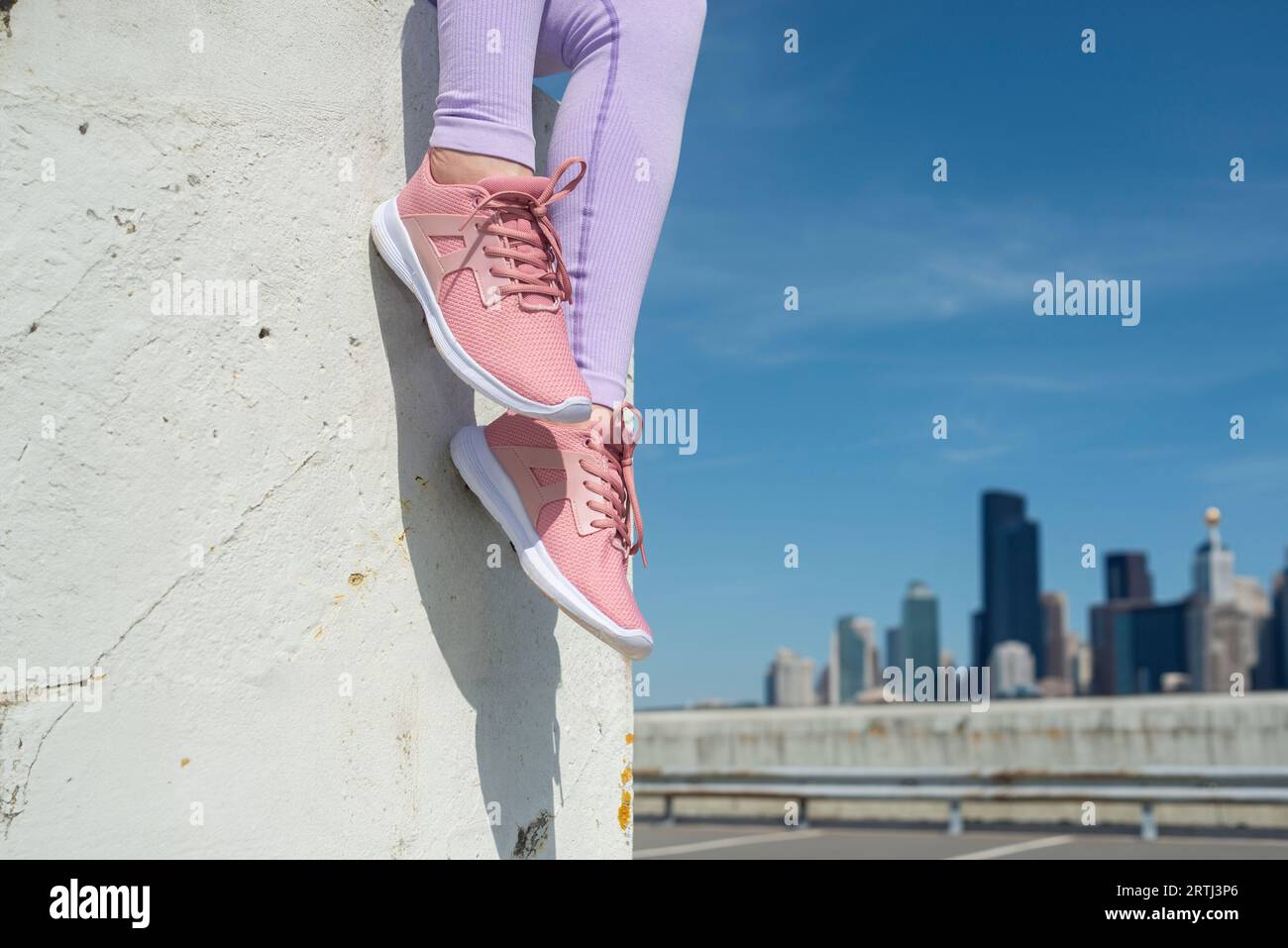 close up of pink trainers against a blue sky and city skyline background, fitness concept Stock Photo