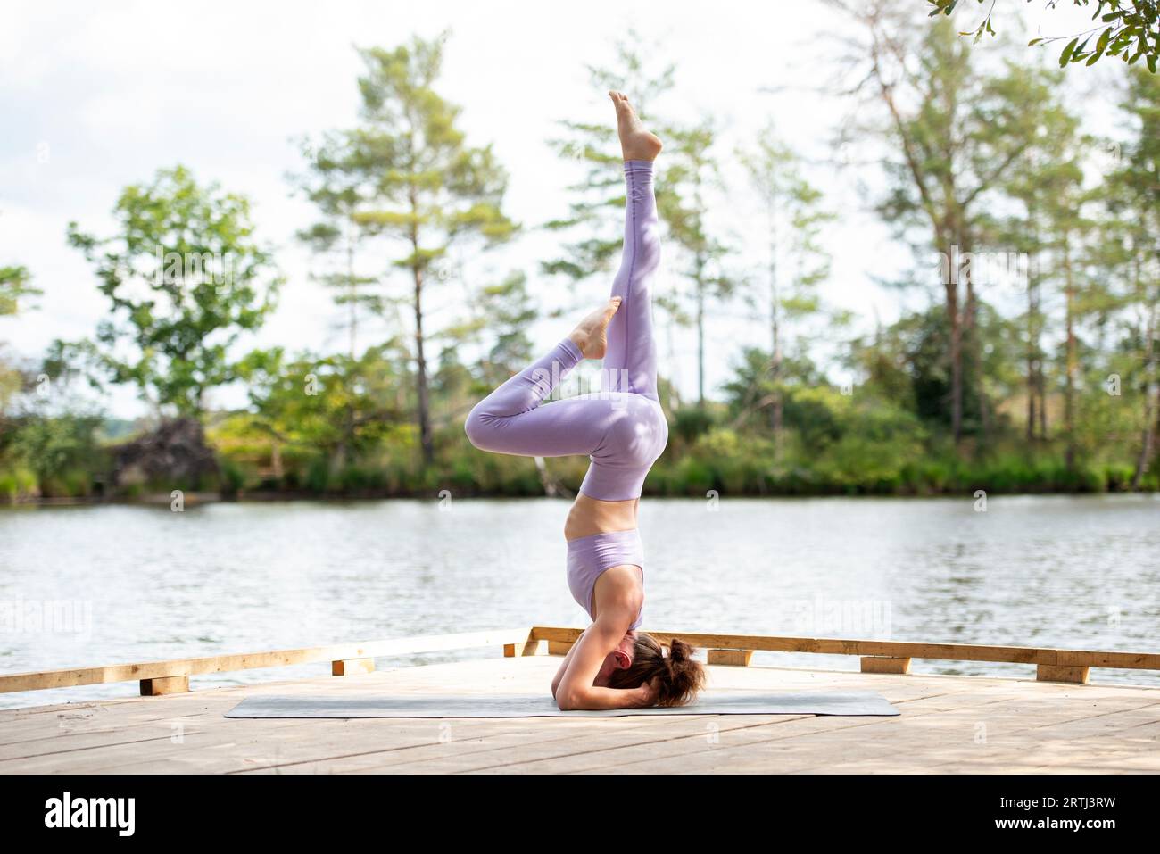 Sporty woman practicing yoga on a jetty by a lake, doing a headstand, part of series. Stock Photo