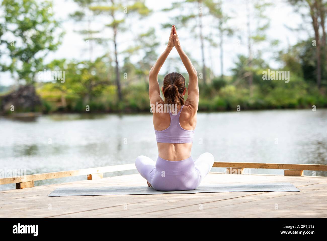 sporty woman practicing yoga on a jetty by a lake, sitting meditating, part of series. Stock Photo