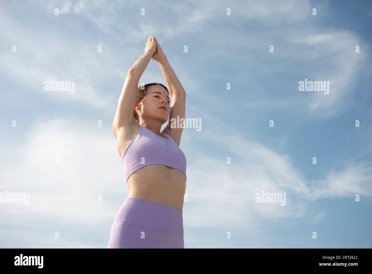 fit, sporty woman engaging in a standing yoga pose with her hands touching above her head. Stock Photo