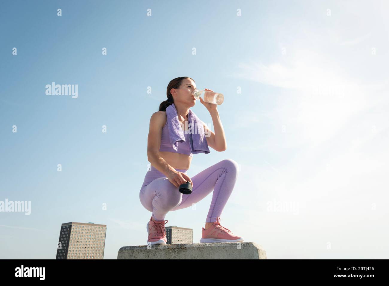 Sporty mid adult woman taking a drink of water from a glass bottle after exercise. Urban background Stock Photo