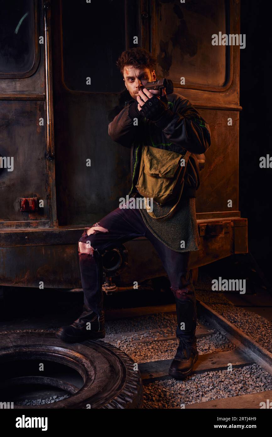 game character in worn outfit aiming with gun in abandoned subway, post-apocalyptic survival Stock Photo