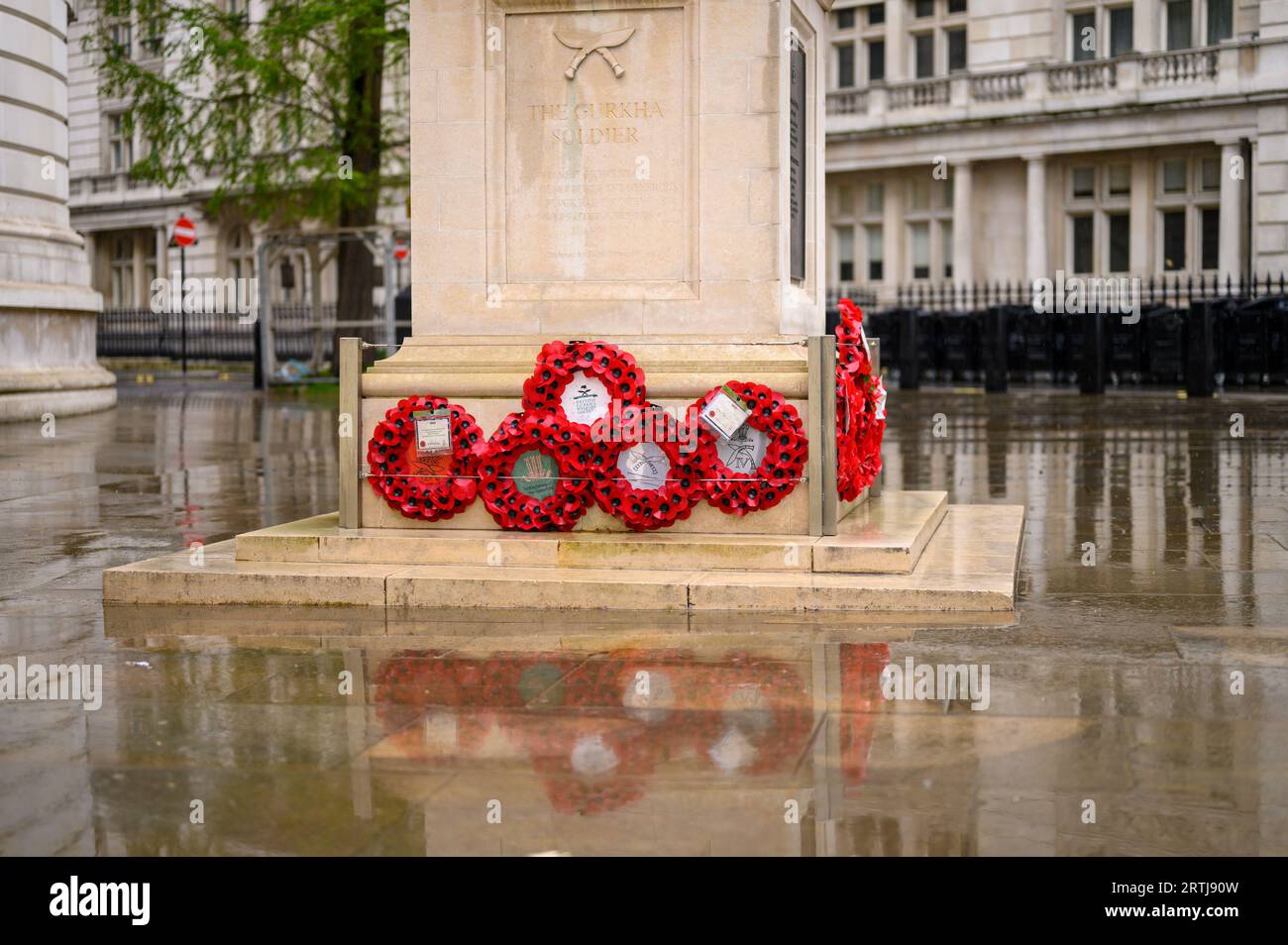 LONDON - April 24, 2023: Red poppy wreaths at the base of the Gurkha soldier statue with reflections on the wet pavement create a poignant scene outsi Stock Photo
