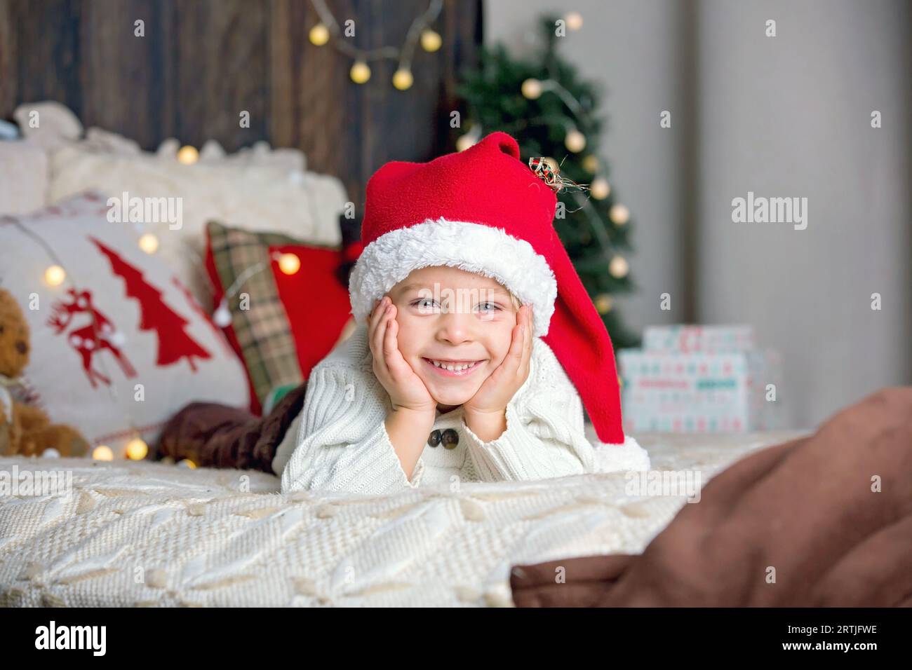 Cute toddler child, boy in a christmas outfut, playing in a wooden cabin on Christmas, derocation around him. Childopening presents Stock Photo