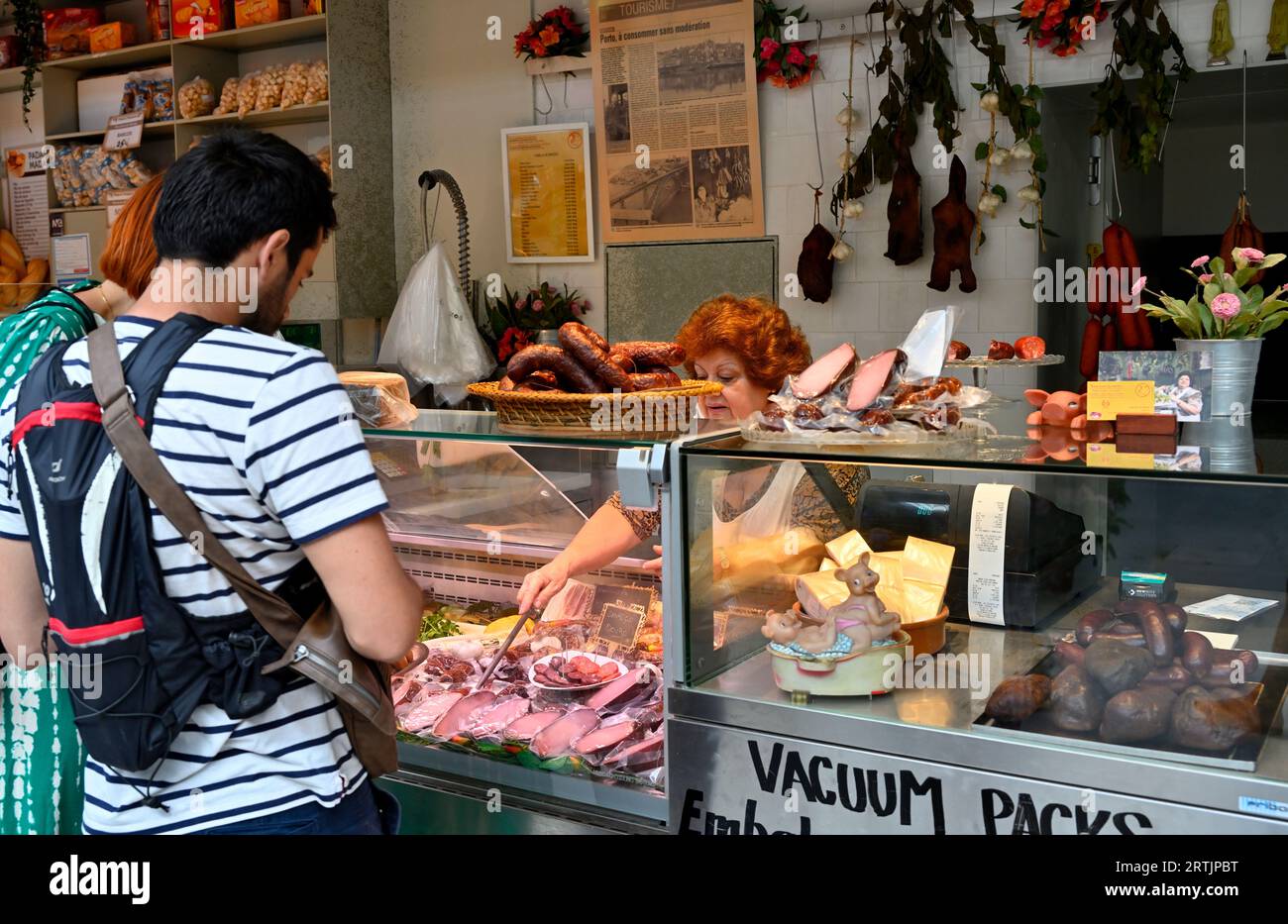 Woman in market stall using good hygiene practice selling variety of sausage and preserved meats serving couple Stock Photo