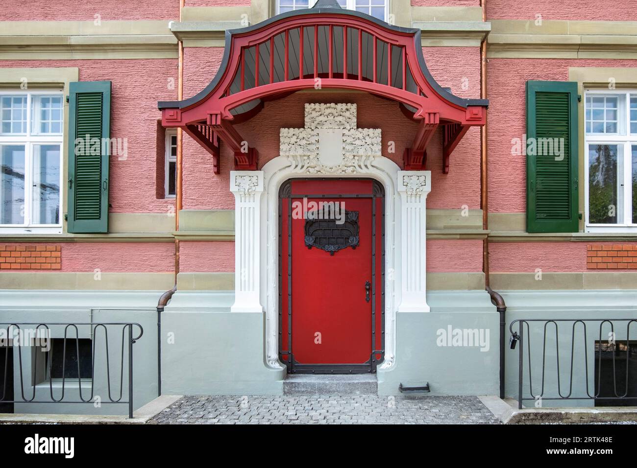 Entrance to secession tenement house. Red front door with decor in Art Nouveau style, retro Swiss urban architecture. City and urban doors. Stock Photo