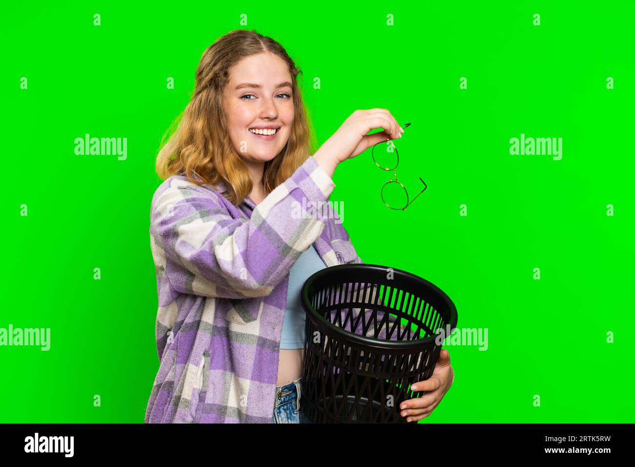 Redhead woman taking off throwing out glasses into bin after medical vision laser treatment therapy surgery looking smiling at camera, heal, cure. Pretty girl isolated on green chroma key background Stock Photo